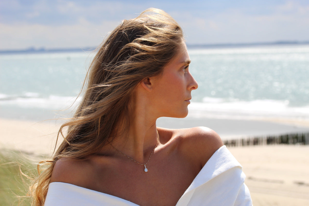 Side view of a woman at the beach wearing the Magic Drop teardrop breast milk pendant on a fine chain