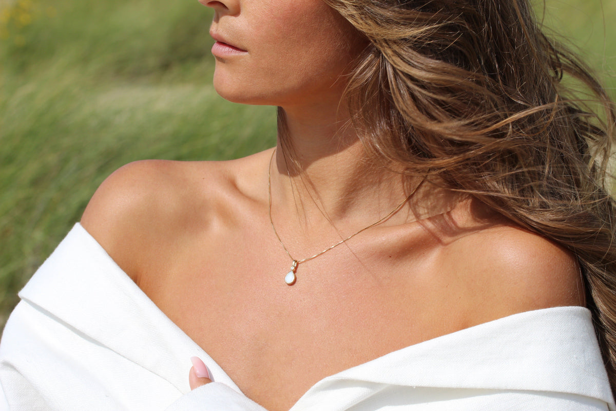 Close-up of the Magic Drop teardrop breast milk pendant on a fine gold chain at the collarbone