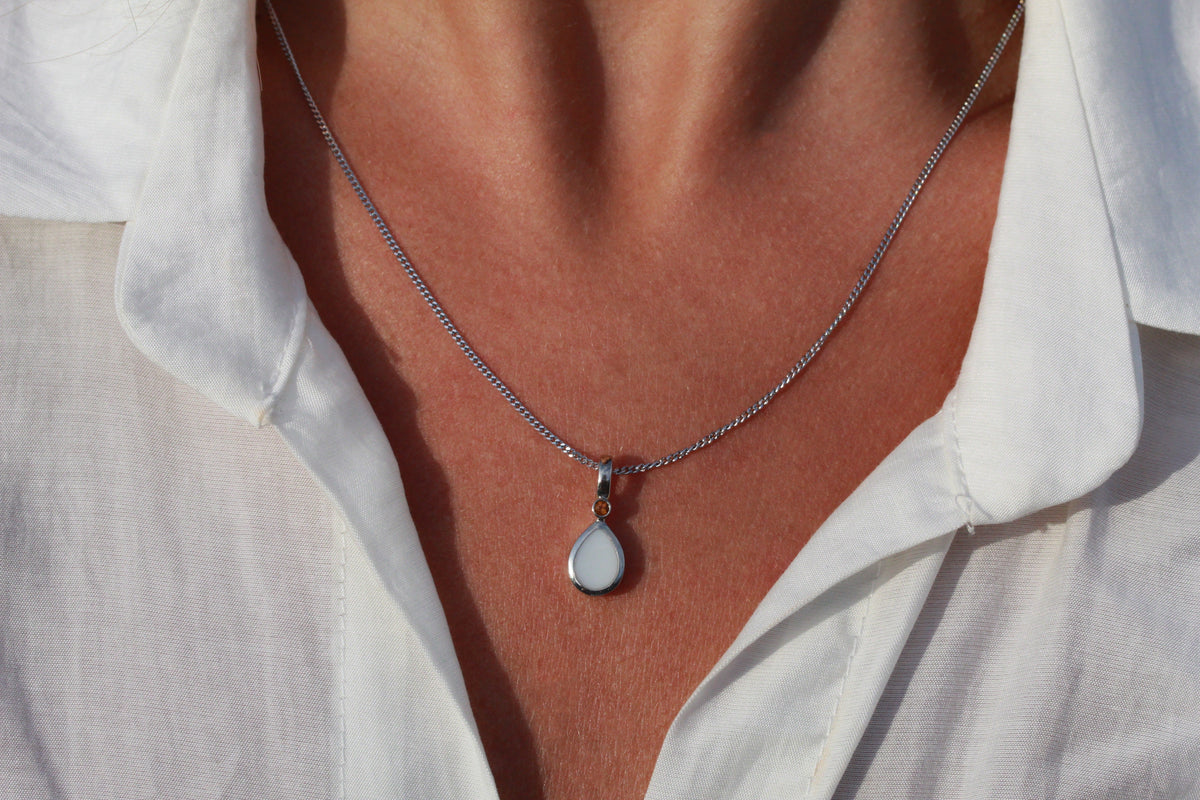 Close-up of a silver-colored Magic Drop teardrop breast milk pendant on a curb chain, worn with a white shirt
