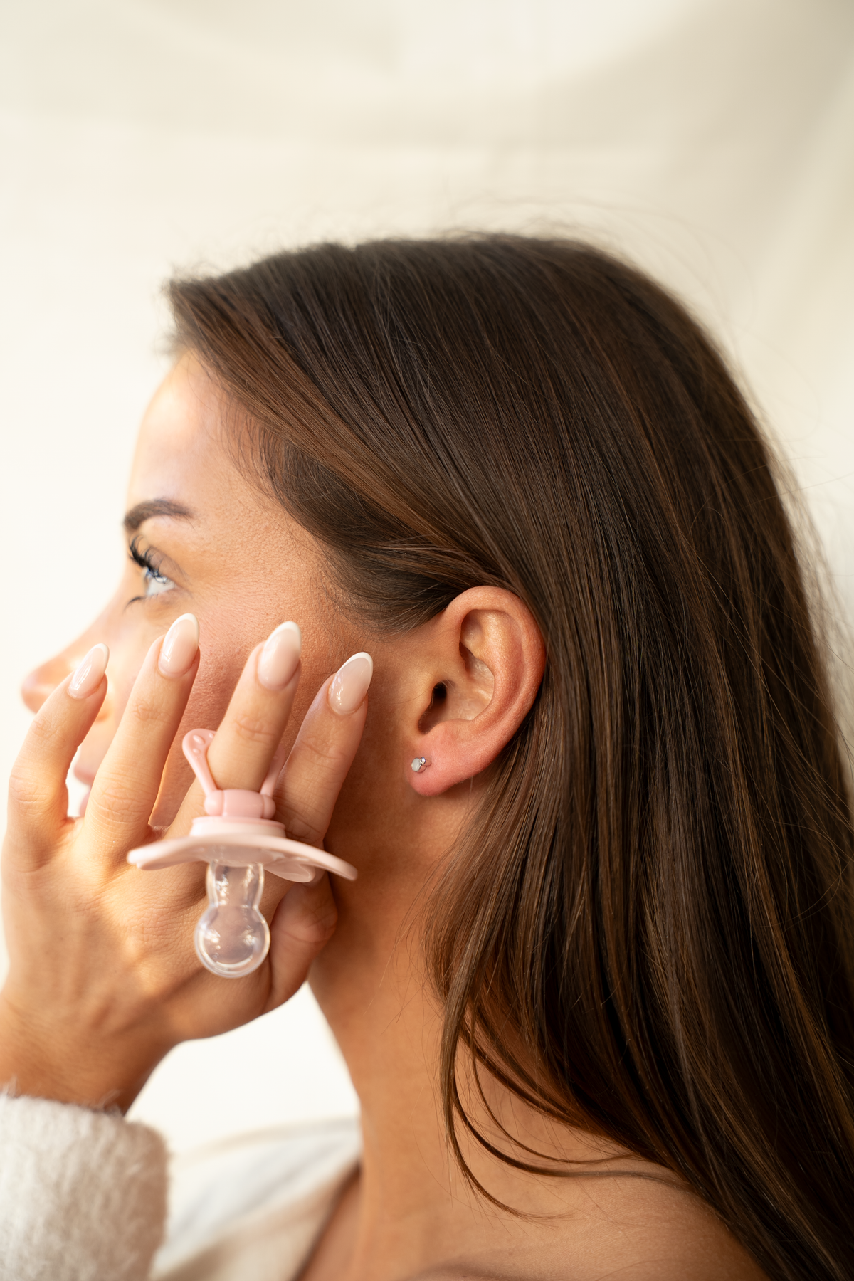 Profile of a woman holding a pink pacifier with a small silver-colored Mila stud in her earlobe