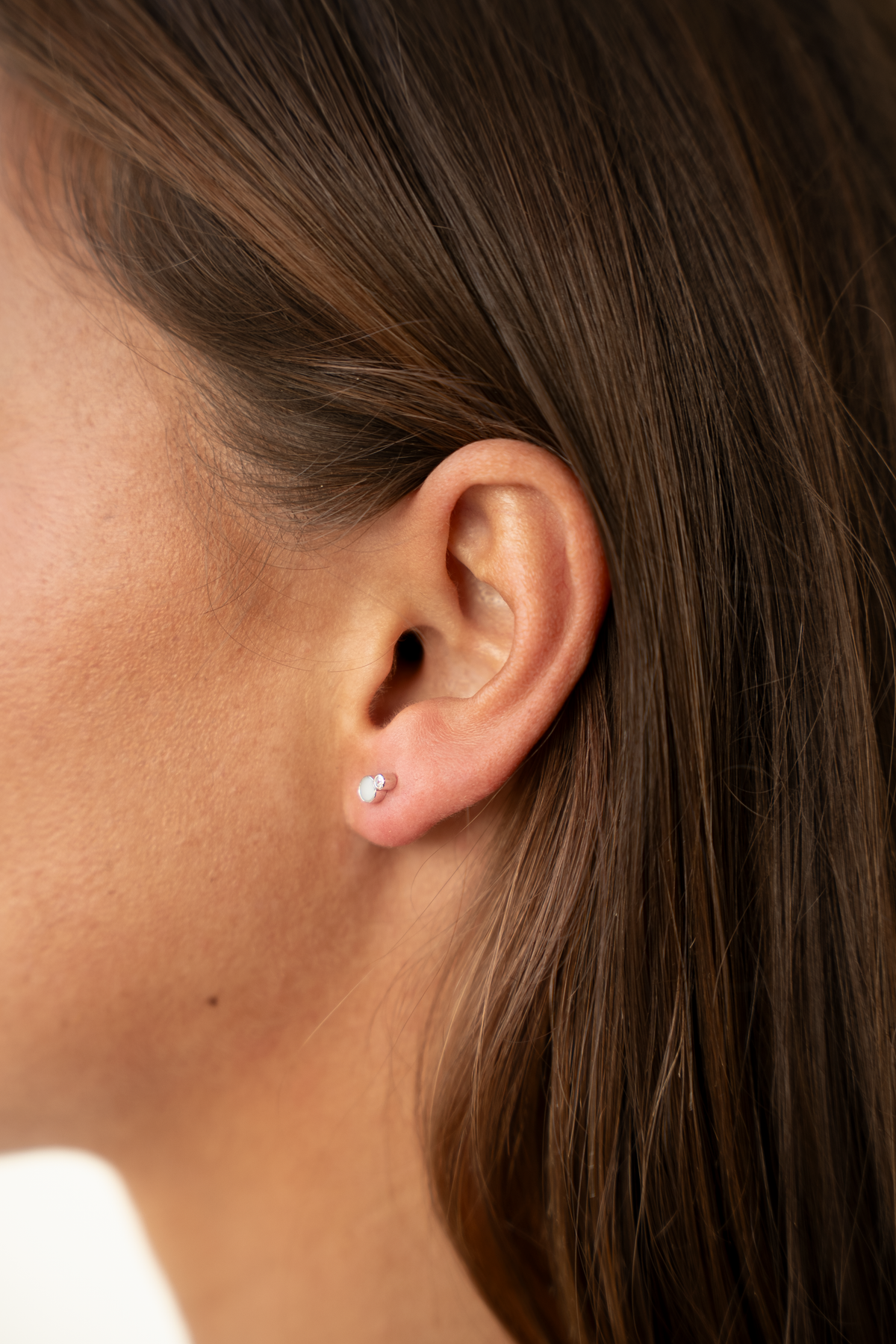 Ear seen from the side wearing a silver-colored Mila stud with a milk stone and clear accent stone