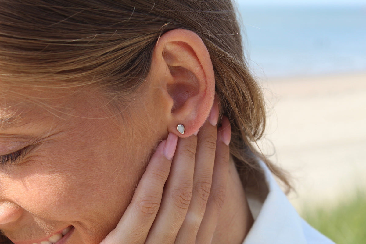 Hand behind the ear of a laughing woman wearing a Mini Drop silver teardrop milk stud