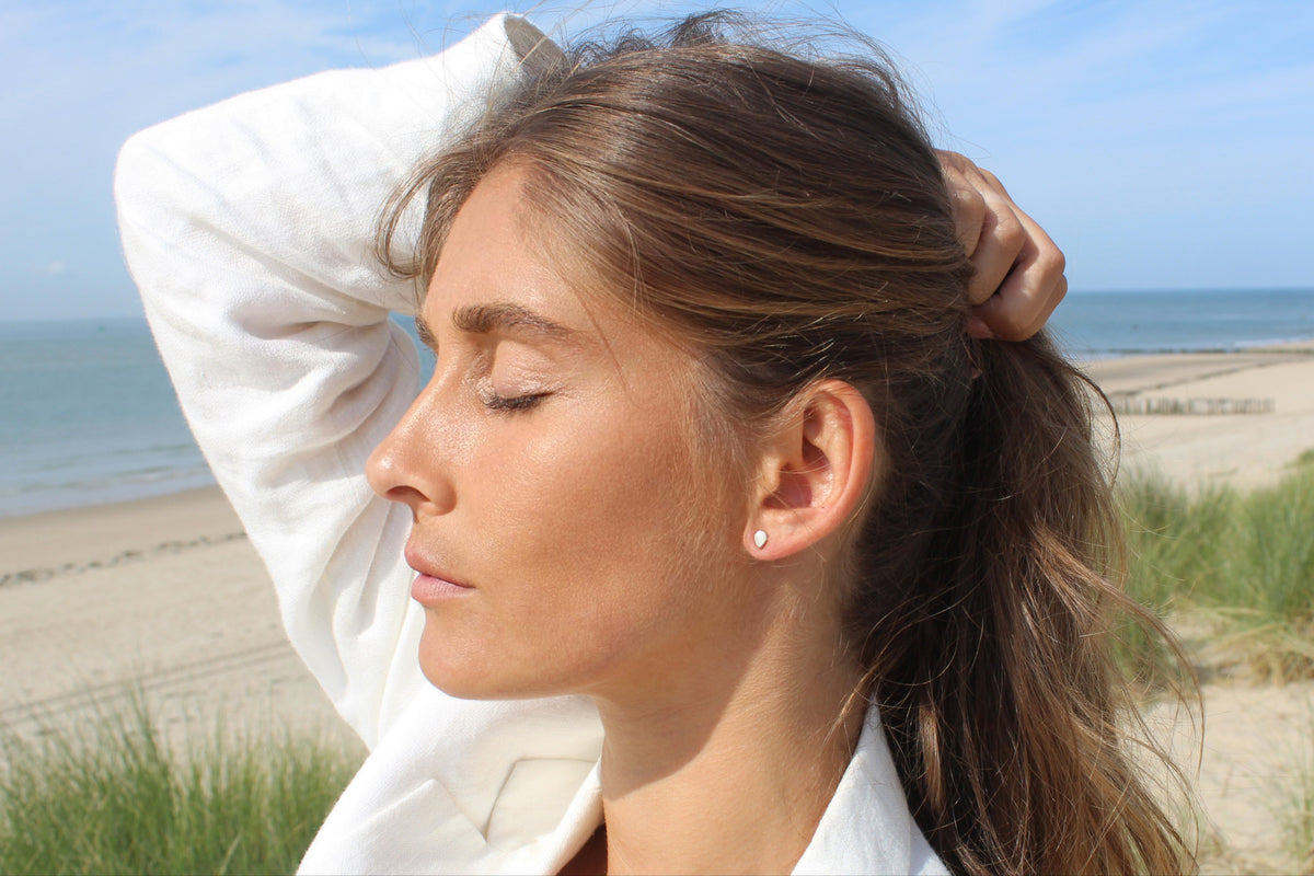 Side profile at the beach with eyes closed, tiny Mini Drop silver teardrop stud on the ear