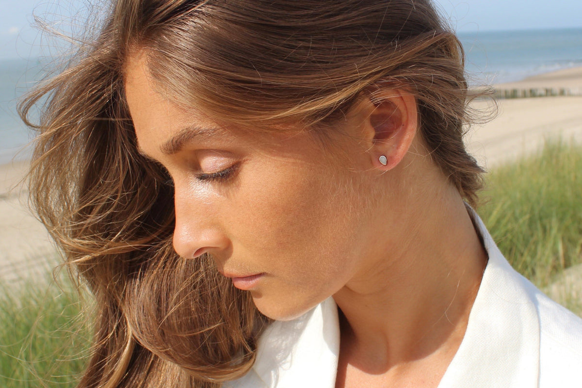 Woman in a white shirt on the dunes, Mini Drop teardrop breast milk stud on her earlobe