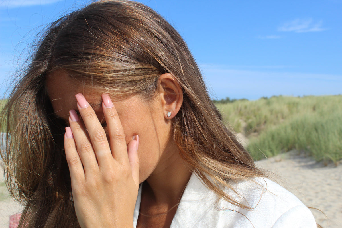 Woman covering her eyes with one hand at the beach, small Mini Drop milk stud visible