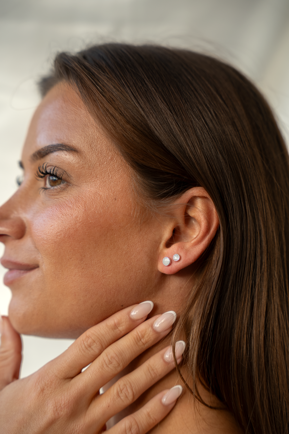 Woman in profile with fingers on her neck, Mini Lis and Lis silver milk studs in one earlobe
