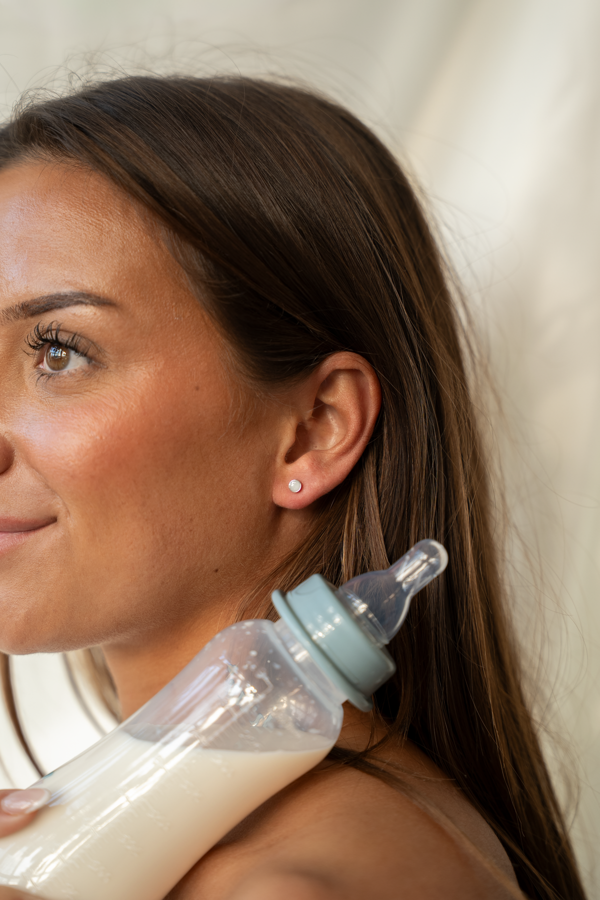 Smiling woman with a milk-filled baby bottle on her shoulder, Mini Lis silver stud in her ear