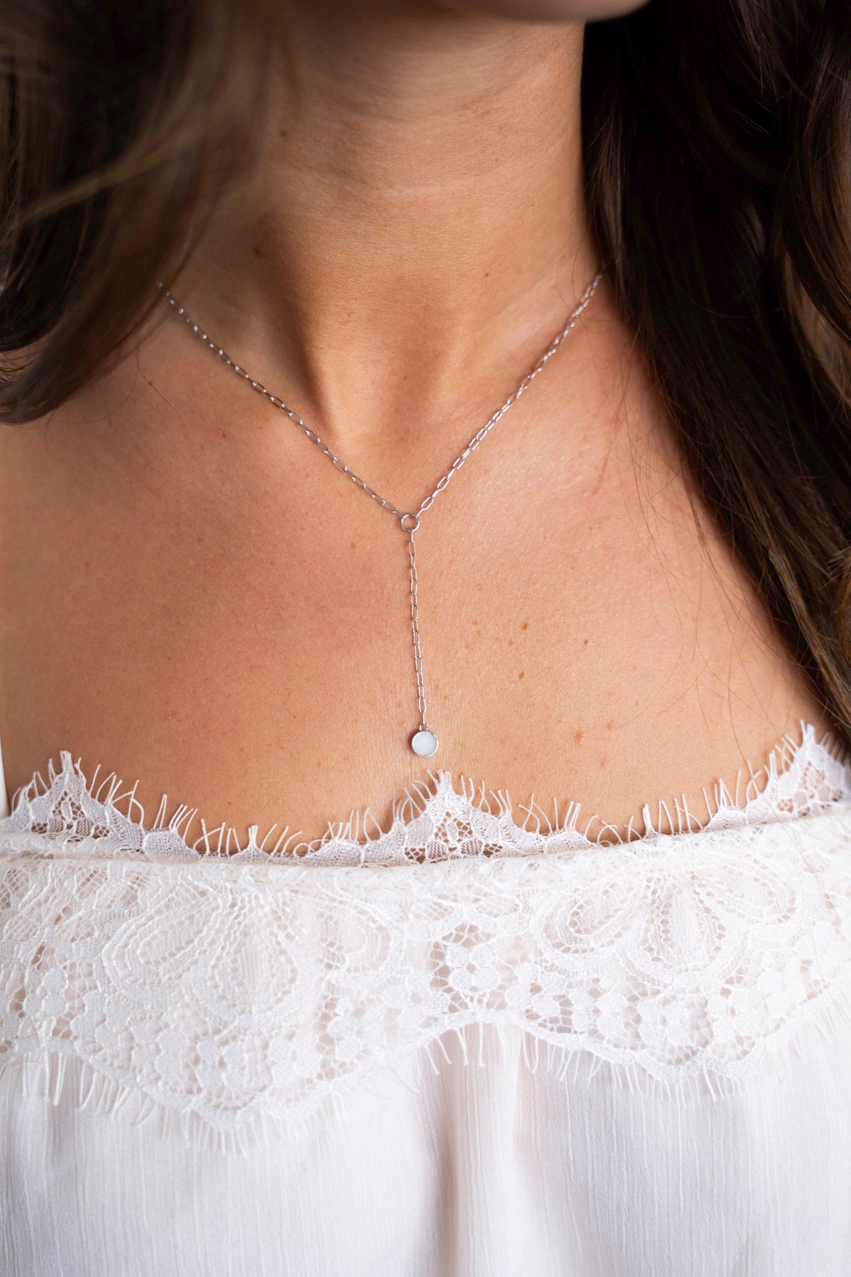 Close-up of the white gold Norah Y-necklace with a round breast milk stone on the décolleté.