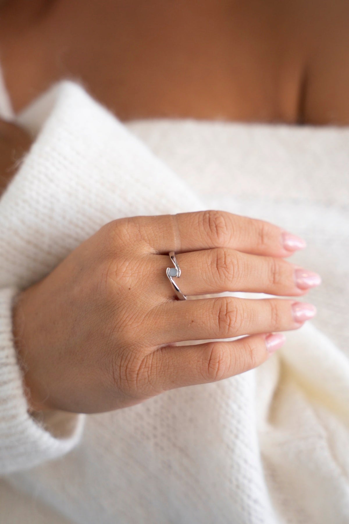 White gold Olivia ring with a small breast milk stone, hand resting on a white sweater.