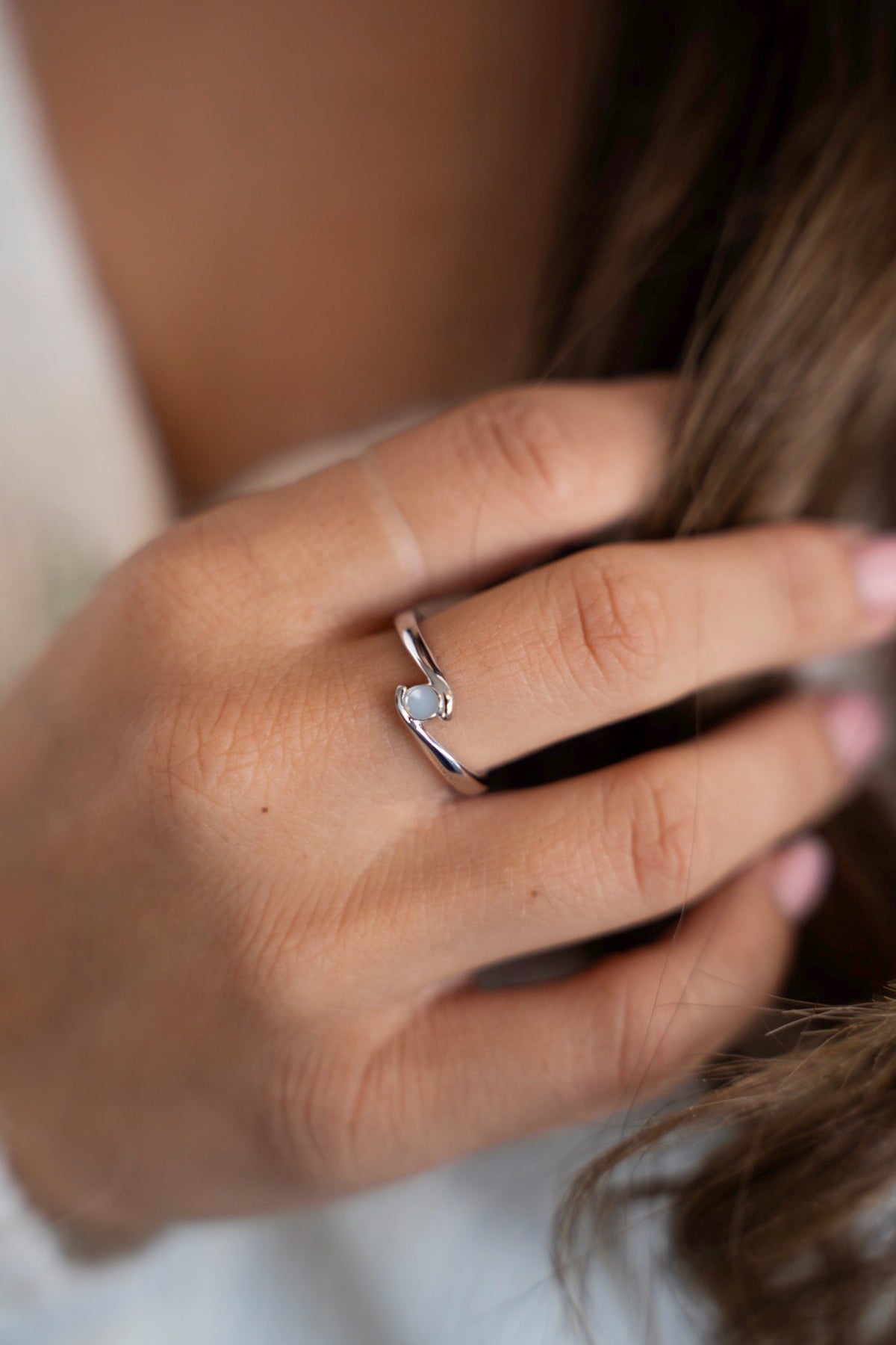 Olivia breast milk ring in solid white gold on a hand in long, wavy hair.