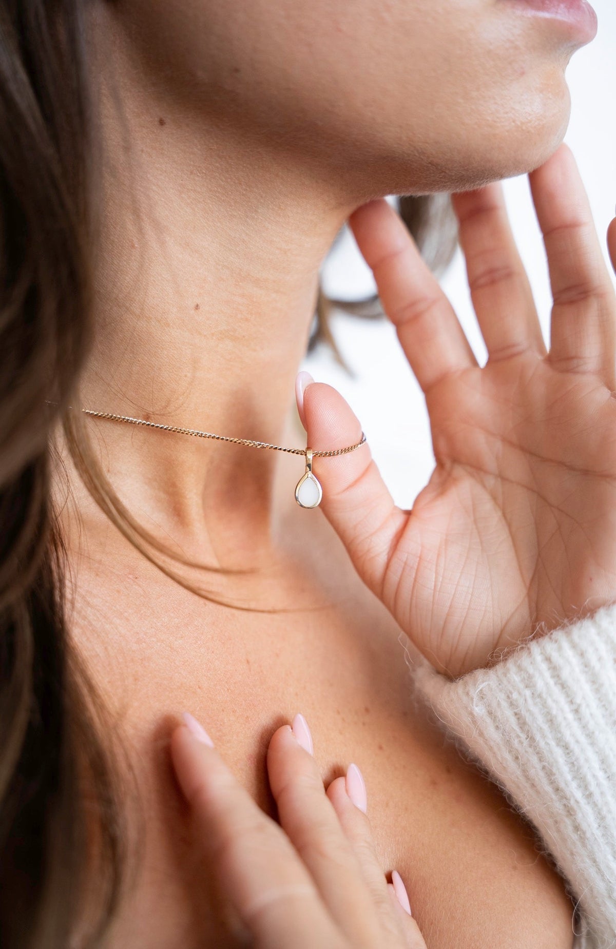 Pure Drop pendant in solid gold with a teardrop-shaped breast milk stone, hand near the neck.