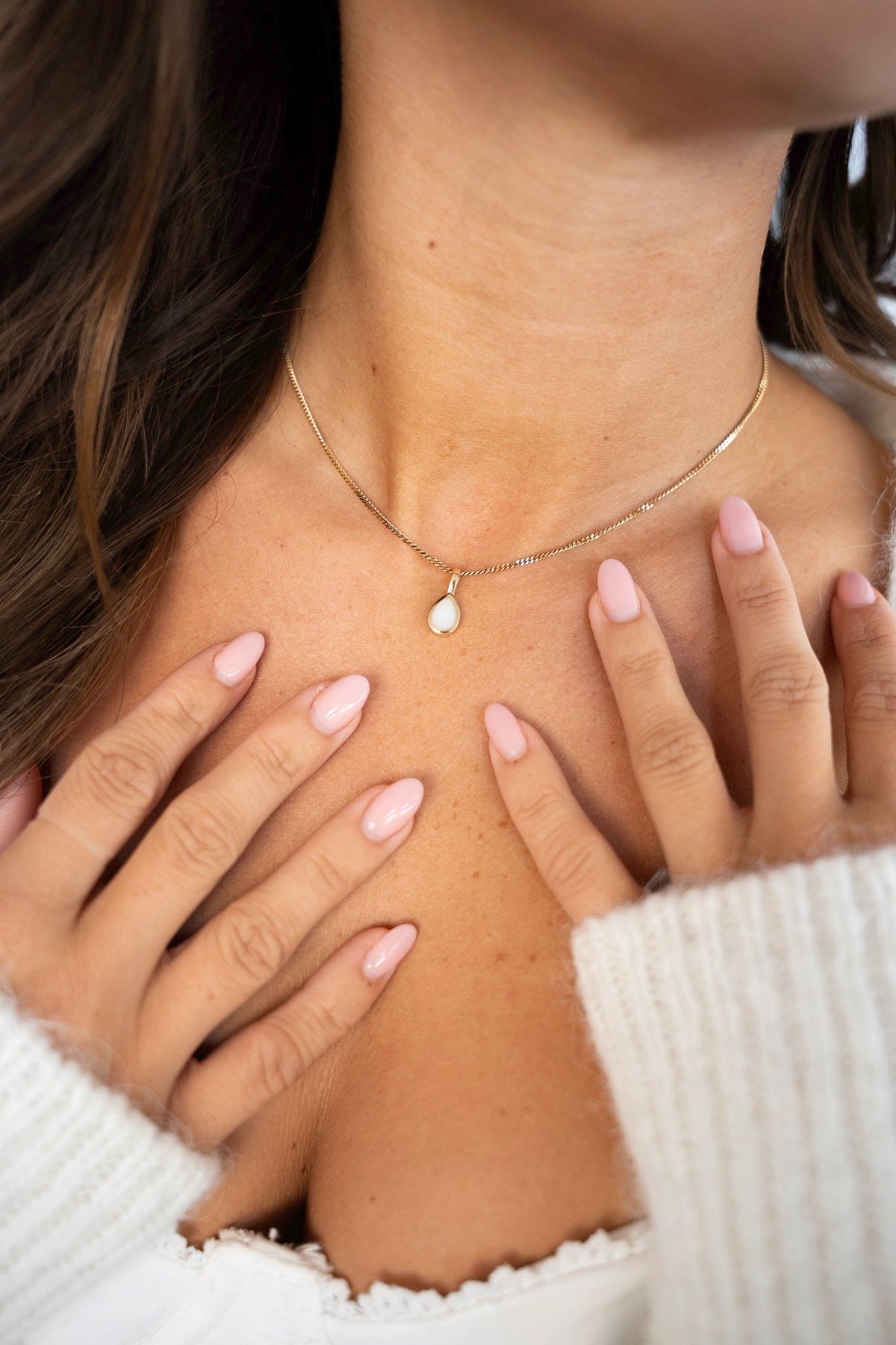 Close-up of the gold Pure Drop pendant with a white breast milk drop, hands on the chest.