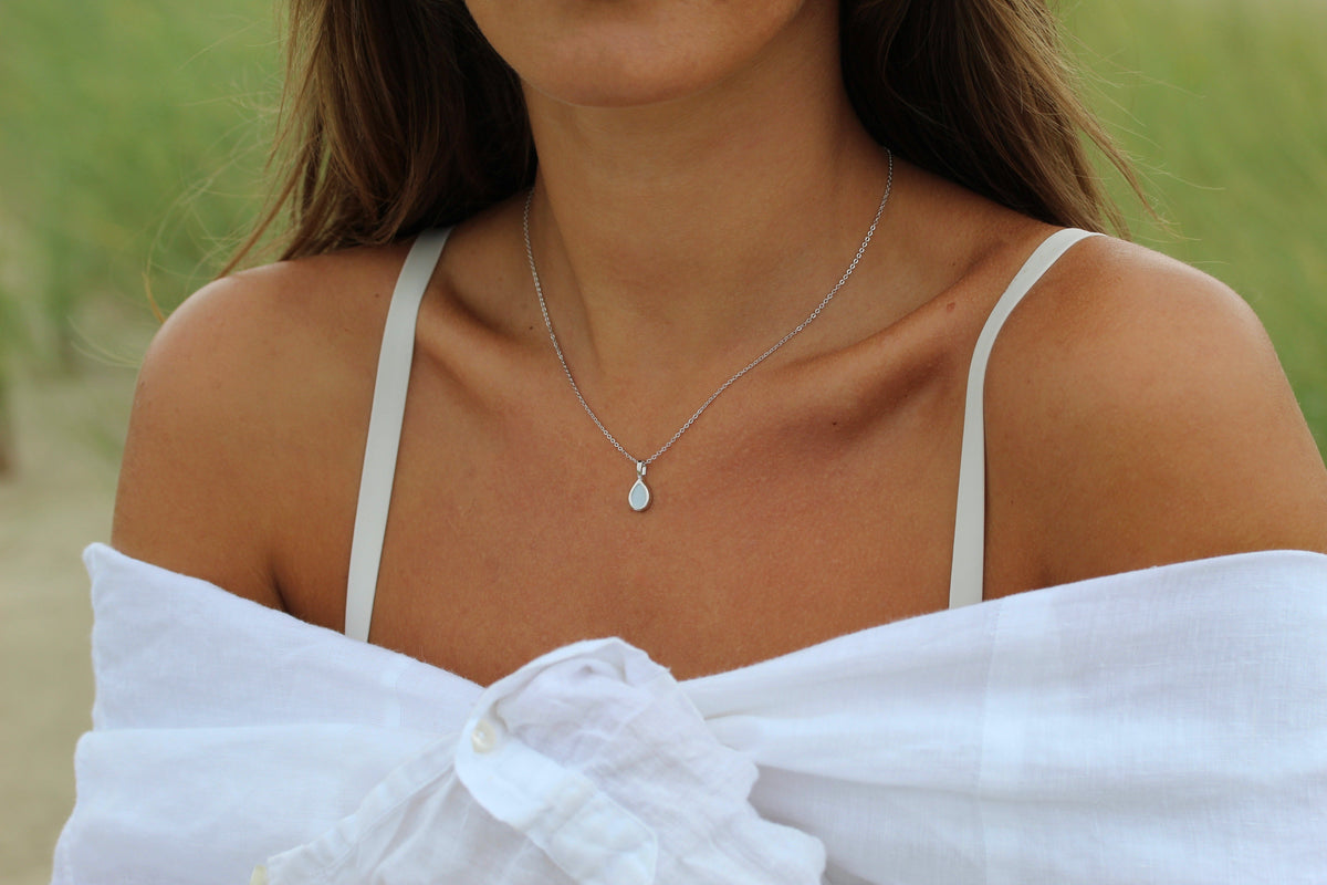 Close-up of a woman wearing the Pure Drop breast milk pendant on a silver-tone chain in the dunes