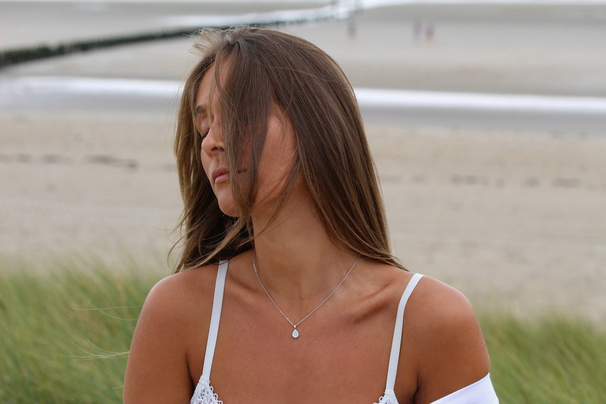 Woman at the beach with hair over her face wearing the silver-tone Pure Drop breast milk pendant