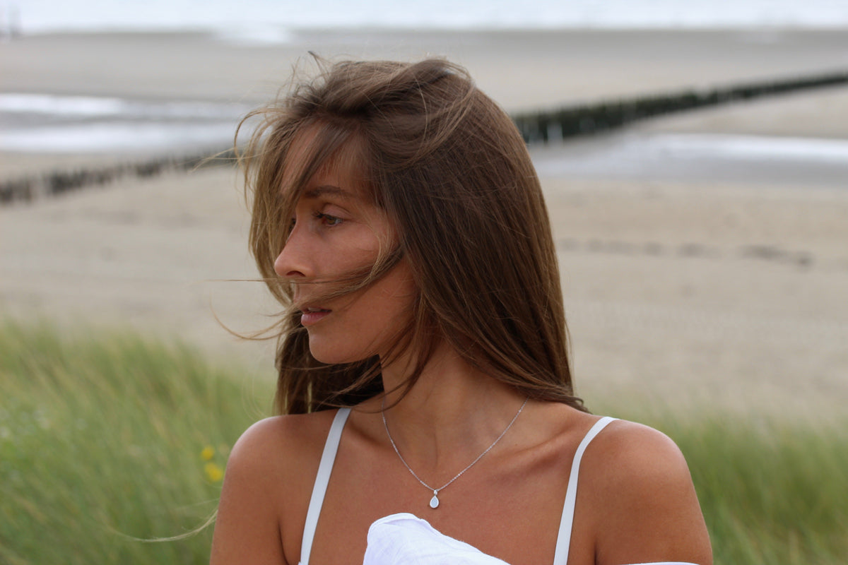 Woman on the beach looking back over her shoulder wearing the silver-tone Pure Drop breast milk pendant