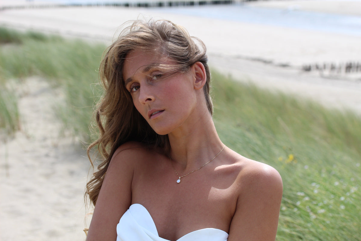 Woman in the dunes wearing the Pure Drop breast milk drop pendant on a thin gold chain