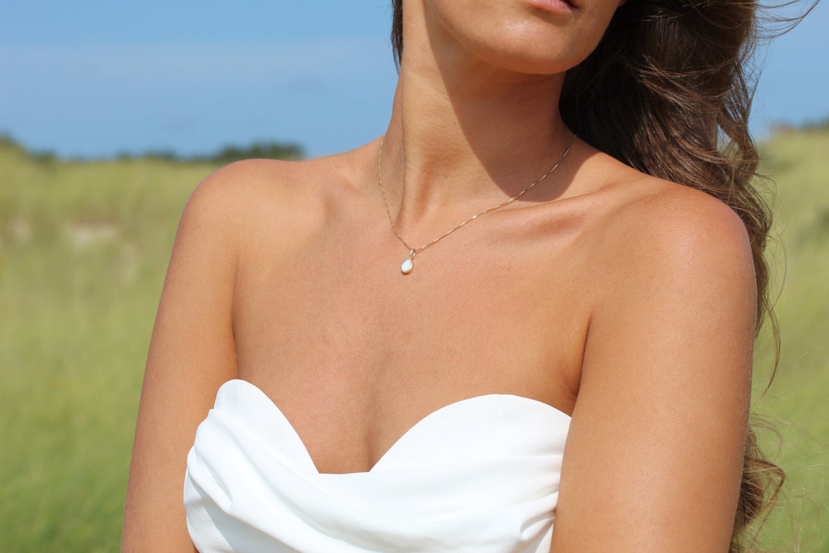Close-up of the Pure Drop breast milk pendant in yellow gold worn with a strapless white top