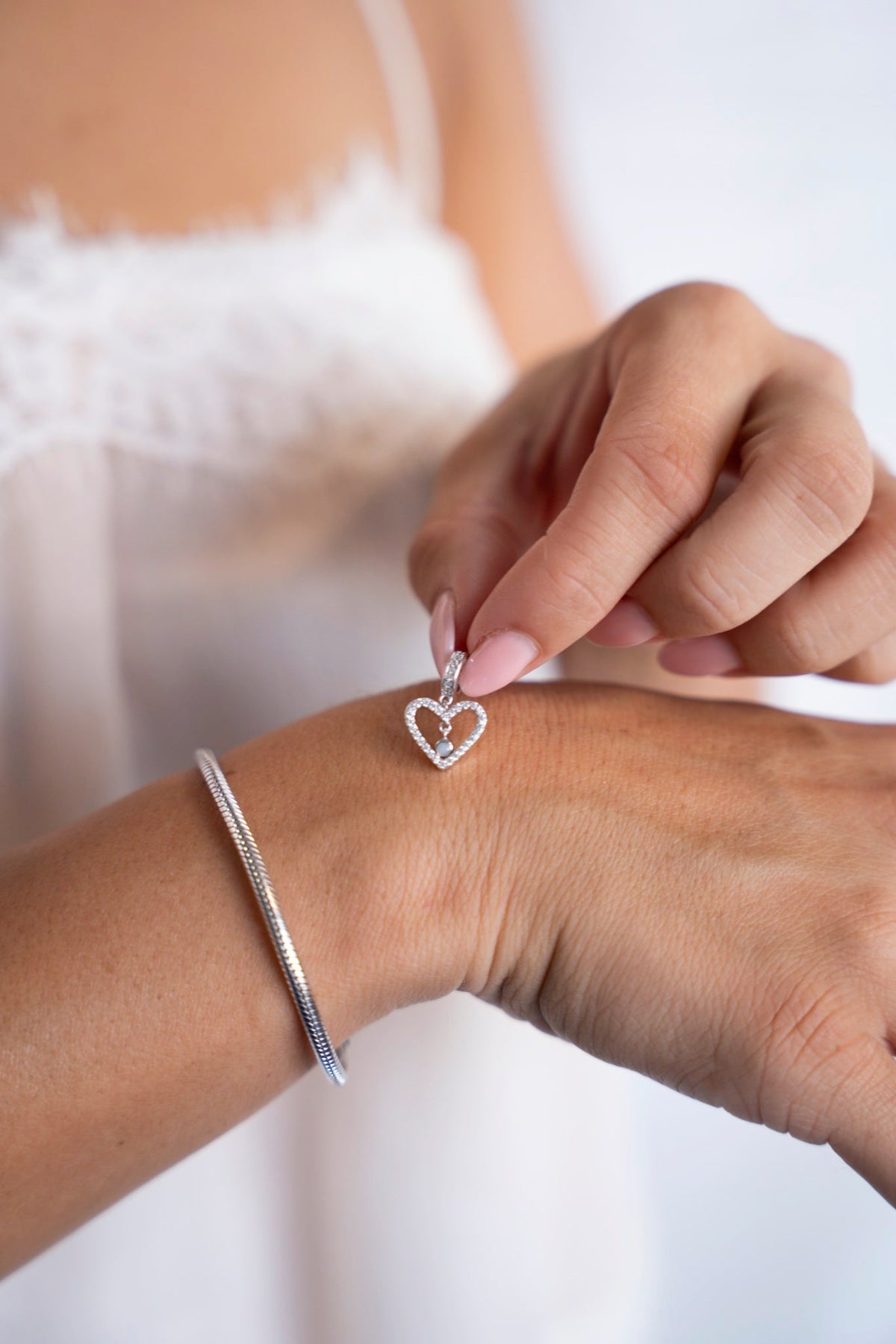 White gold Sophie heart charm with breast milk, next to a bracelet on the wrist.