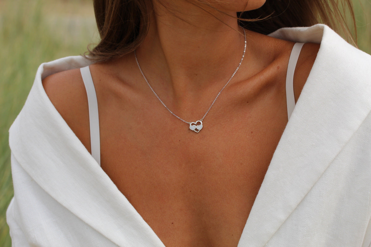Close-up of a silver-colored Trinity necklace with two breast milk hearts inside an open heart