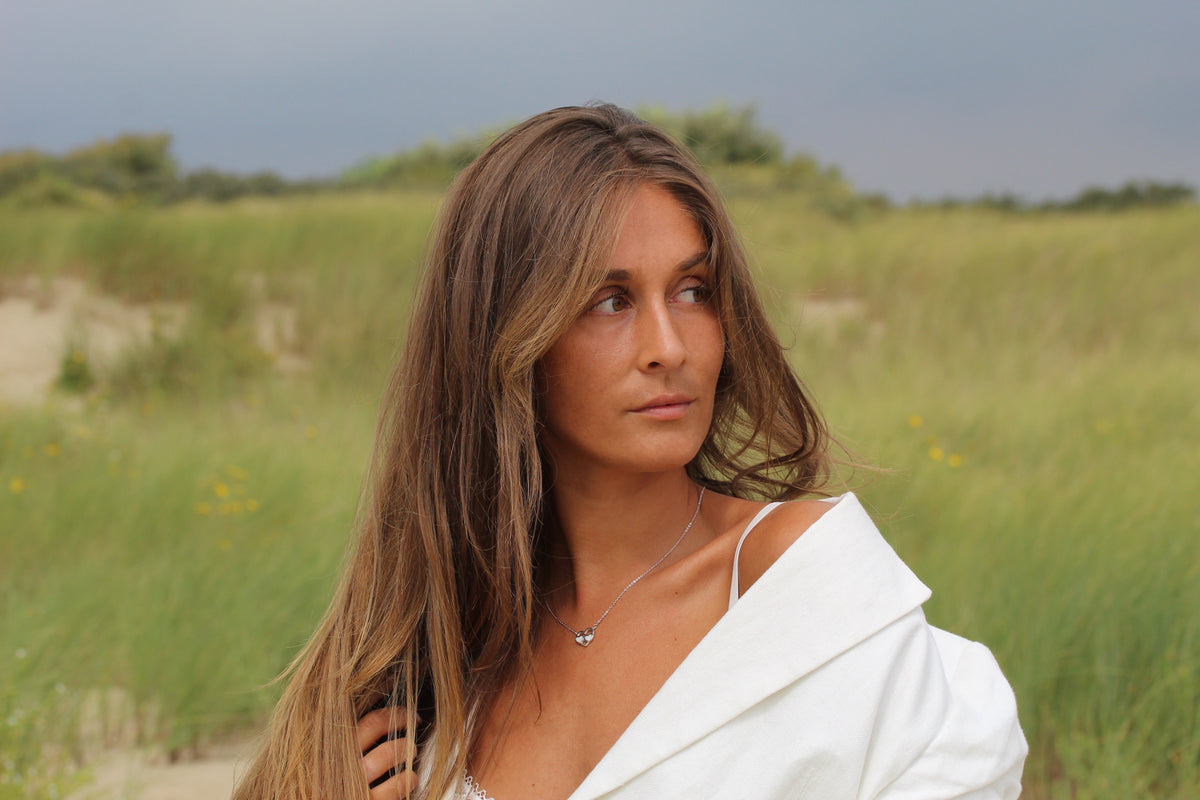 Woman in a white top in the dunes wearing a silver-colored Trinity heart breast milk necklace