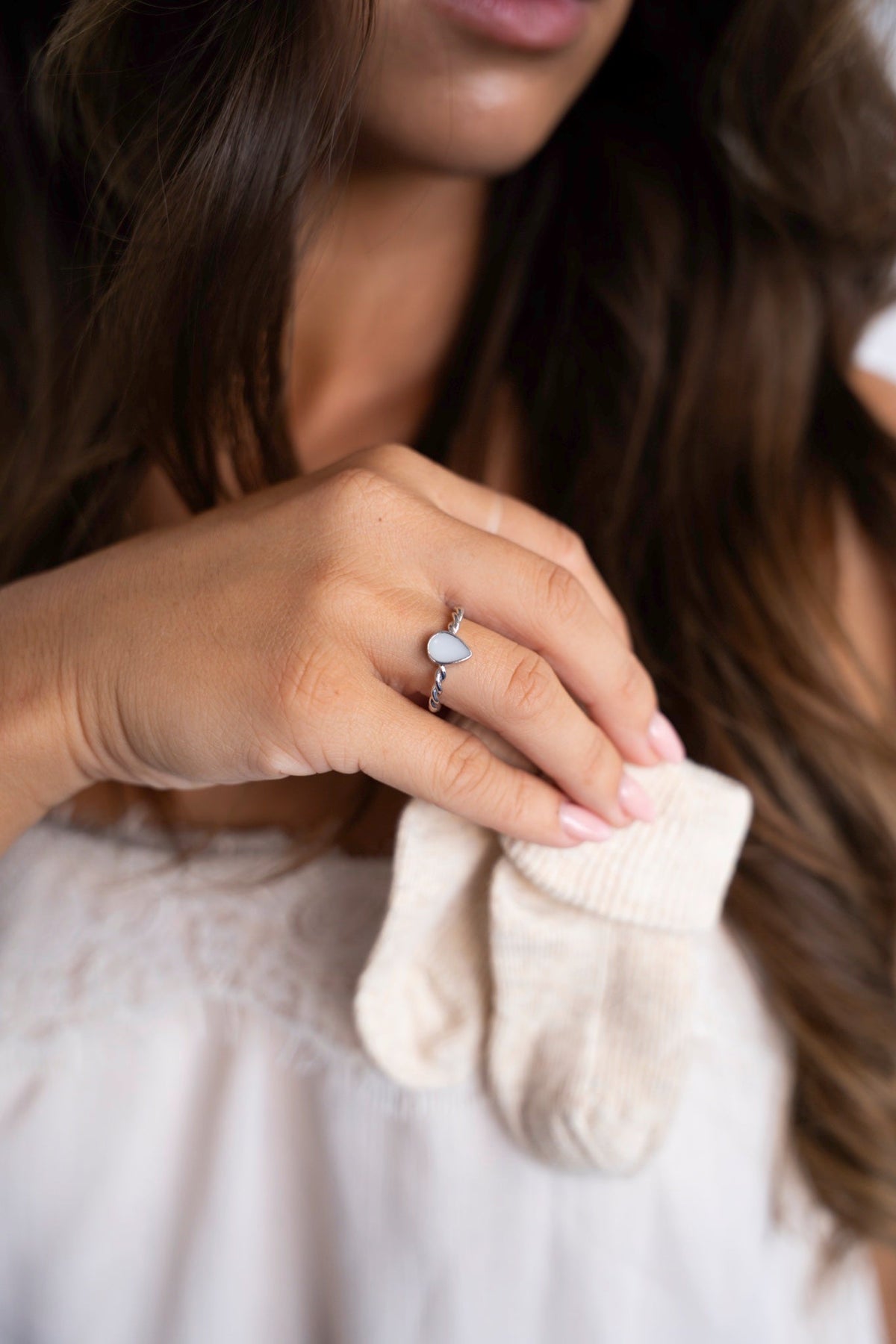 Silver Turning Droplet ring with a teardrop-shaped breast milk stone, hand holding baby socks.