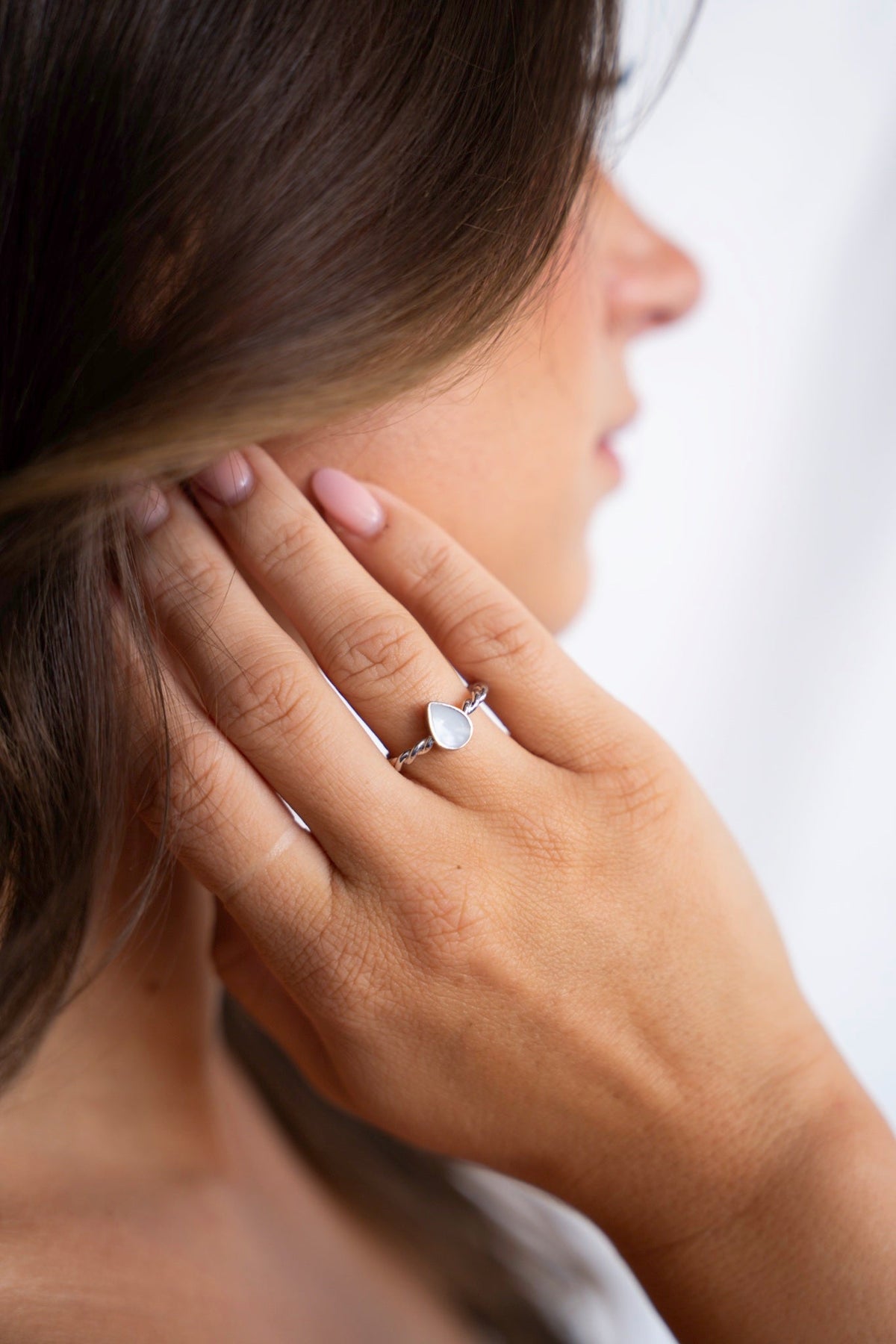 Hand near the ear wearing the Turning Droplet breast milk ring in 925 sterling silver.