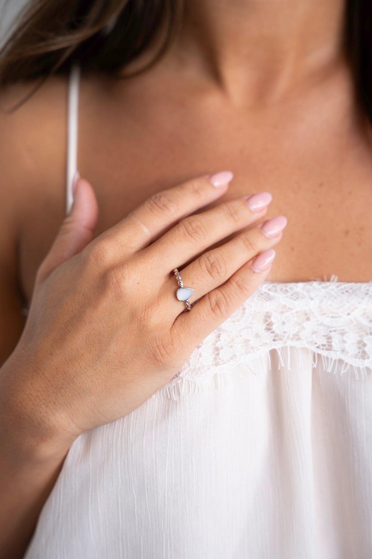 Hand on the chest wearing the silver Turning Droplet ring, above a white lace top.