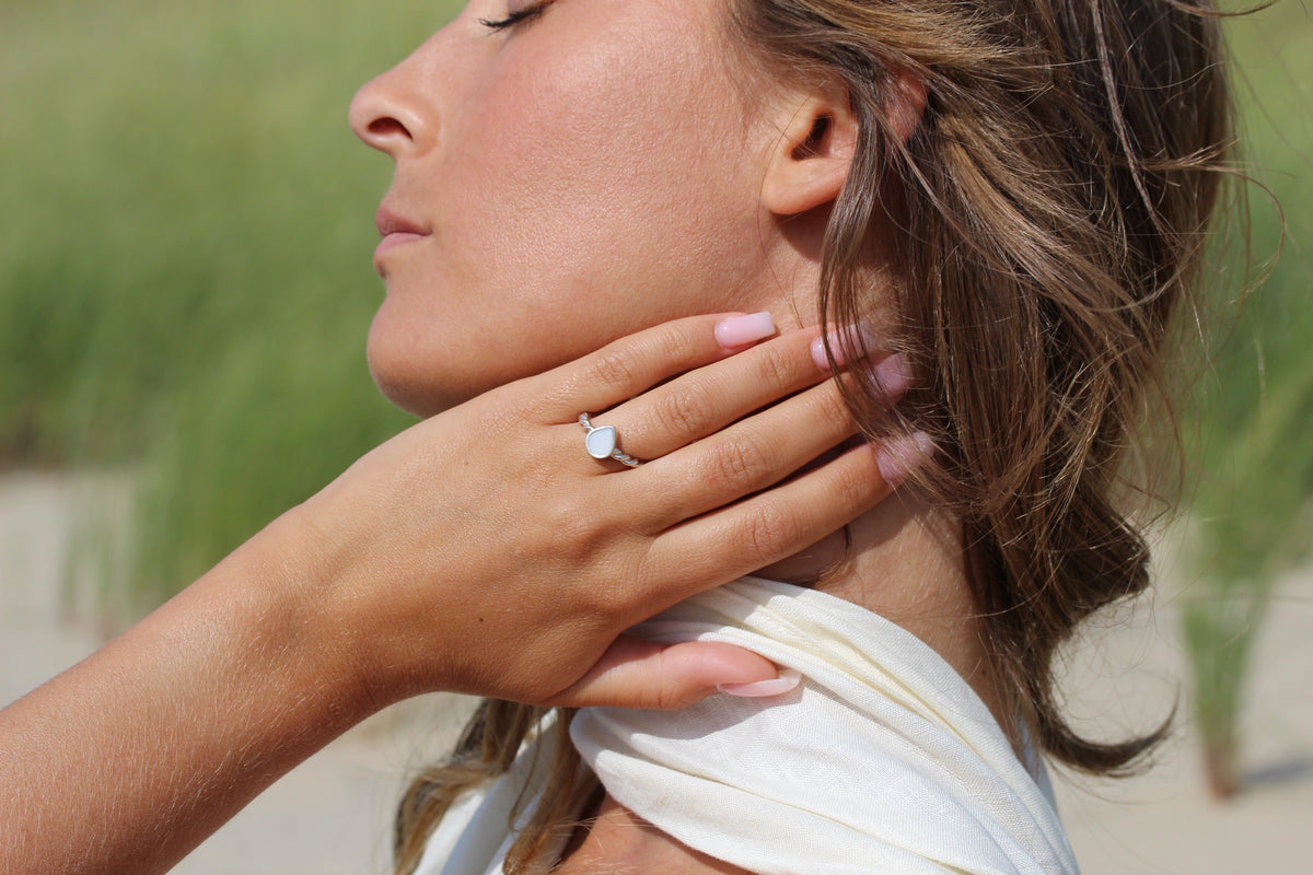 Silver Turning Droplet breast milk ring on the finger, hand on the neck with a cream scarf, dunes behind