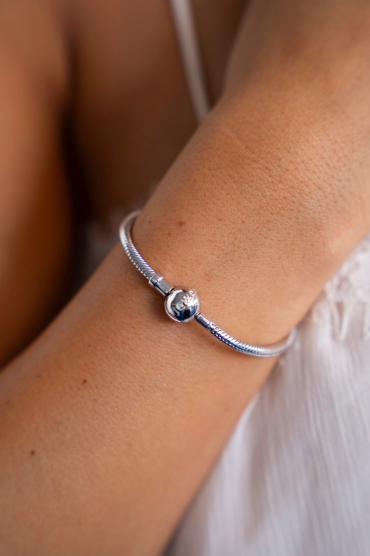 Close-up of the silver charm bracelet with snake chain and round clasp on the wrist.
