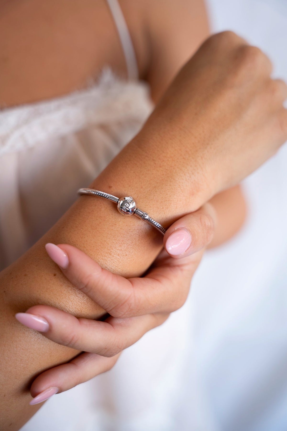 Charm bracelet in 925 sterling silver on the wrist, the other hand holding the arm.